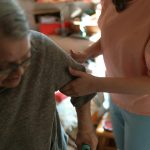 Compassionate caregiver helps elderly woman with mobility at home, offering caring support.